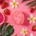 Sorbet Ruby Berry Island Way dans sa coque d’orange, posé sur un fond rose tropical avec fleurs et fruits frais